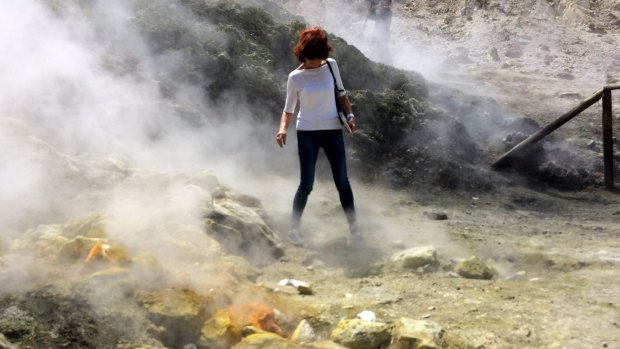 A woman takes a close look at a steaming fumarola at the Solfatara crater bed in the Campi Flegrei near Naples, Italy. 