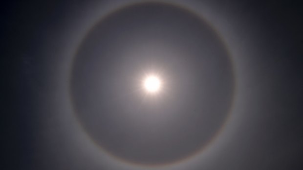 A halo around the sun appears just before midday. The red line on its inside is because red light bends slightly less than blue light. 