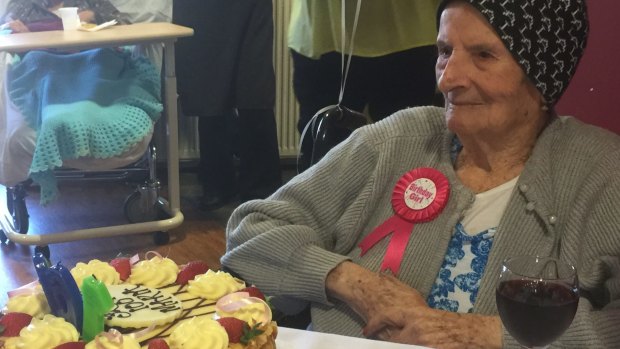 Maria Stella Costa marks her 100th birthday with a cake - one of three - and a glass of red.