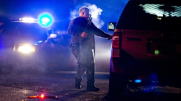 An Oregon State police officer stands by a vehicle as police officers block Highway 395 in Seneca, Oregon, on Tuesday.