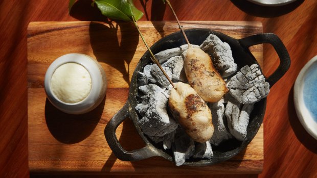 Potato damper skewered on baby eucalyptus leaves, cooking directly against hot coals right at your table.