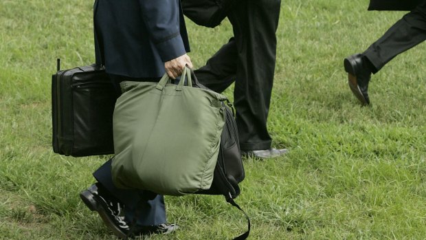 A member of the US military carries the "football," the case in his left hand, as he walks behind President George W. Bush on the South Lawn of the White House in 2005.