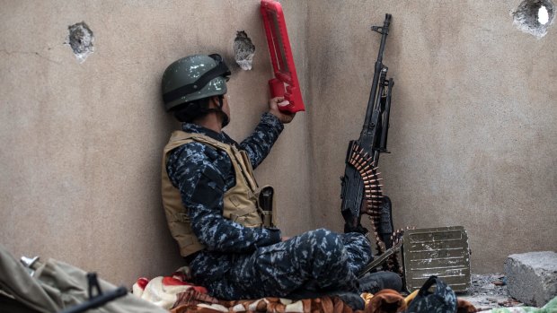 An Iraqi policeman uses a mirror to try to spot a sniper during the battle to recapture Mosul.