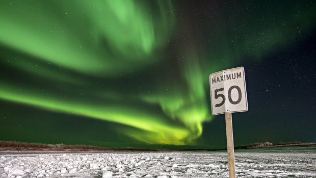 The northern lights illuminate the night sky above a road sign in Inuvik, Northwest Territories, Canada.