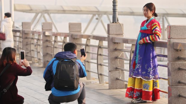 A Chinese tourist in a traditional Korean costume on the bank of Yalu River.