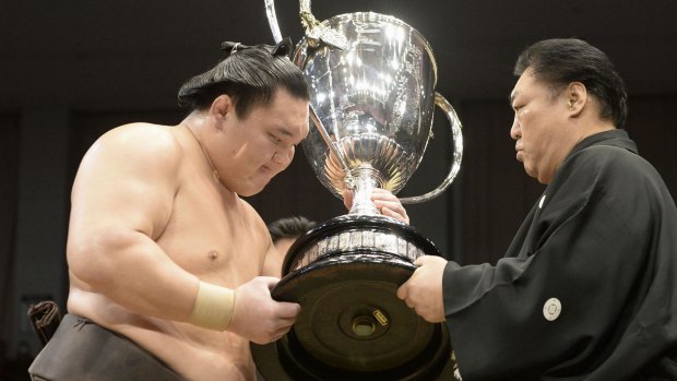 Mongolian grand champion Hakuho (left) receives the trophy from Kitanoumi, chairman of the Japan Sumo Association.