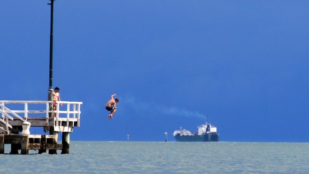 Young men jump from a pier into Port Phillip Bay.