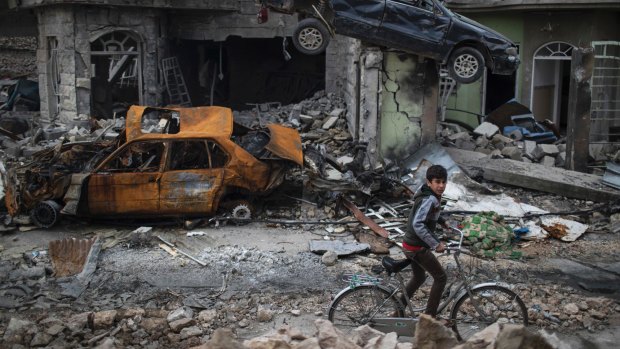 The broken city: a boy rides past destroyed cars and houses in a Mosul neighborhood recently liberated by Iraqi forces.