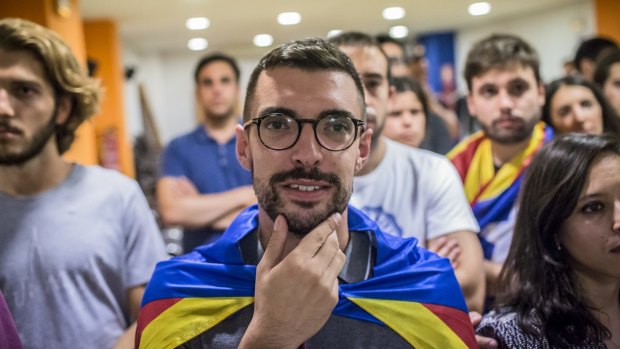 Members of the Young Nationalists of Catalonia (JNC) watch as Catalonia's president makes a televised speech.