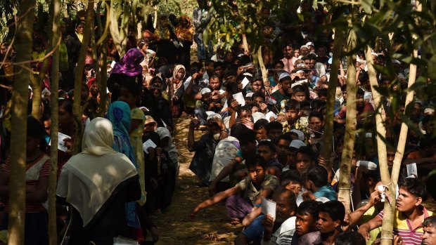 Rohingya refugees sit in a queue at a Red Cross distribution point.