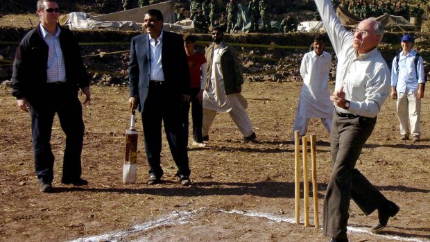 John Howard (right) bowls a cricket ball in Pakistan, and trips shortly afterwards.
