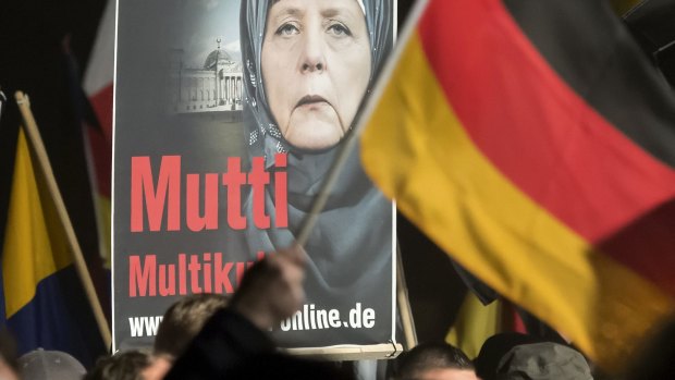 A banner reading 'Mum multiculti' and depicting a manipulated image of German Chancellor Angela Merkel is carried by a protester behind the German flag as thousands of people join a protest in Erfurt, central Germany, on Wednesday. 