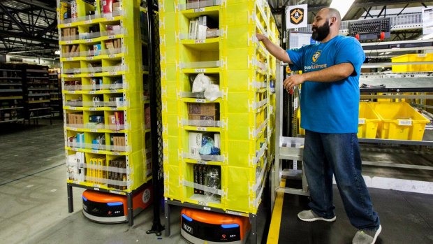 An Amazon staff member picks items from a rack brought to him by a Kiva robot.