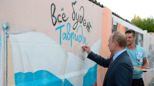 Russian President Vladimir Putin signs  graffiti showing a Russian state flag and text reading 'All will be well. Tavrida', as he visits the youth educational forum 'Tavrida' in Crimea earlier this month.