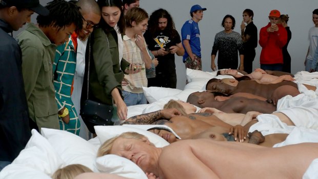 Visitors, including Kendall Jenner, admire Kanye West's sculpture of naked celebrities, with a slumbering Donald Trump in foreground.