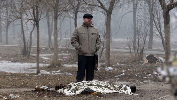 A man stands beside the covered body of a man killed in the shelling of Mariupol on Saturday.