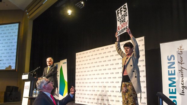 A protester holds up her sign while Malcolm Turnbull halts his speech.