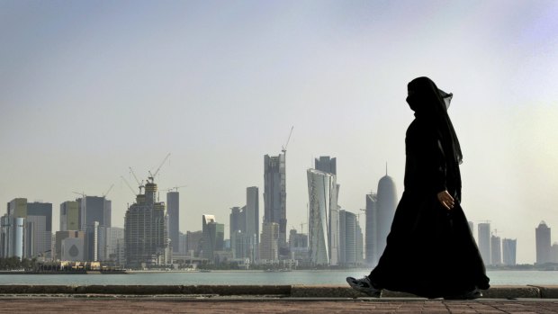 A Qatari woman walks in front of the city skyline in Doha. .
