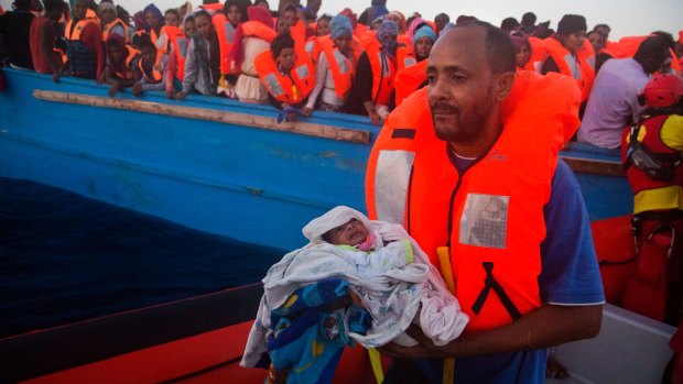 A man carries his five-day-old son after been rescued from a crowded wooden vessel as they were fleeing Libya.