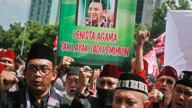 Muslim protesters shout slogans as they hold up a placard with a picture depicting Jakarta governor Basuki "Ahok" Tjahaja Purnama behind bars.