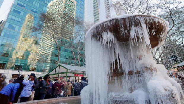 People pose for photographs in front of a frozen water fountain at Bryant Park, in New York.