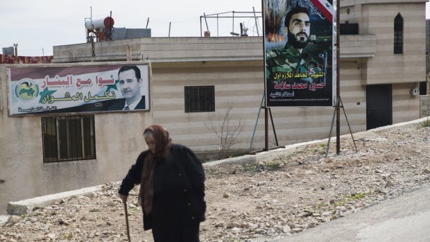 A woman passes banners with a portrait of Syrian President Bashar al-Assad, left, and a killed Syrian officer on a road near Latakia.
