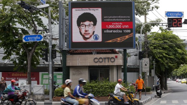 People ride past a digital billboard showing a sketch of the main suspect in the Erawan shrine bombing. 