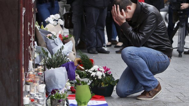 A man holds his head in his hands as he lays flowers in front of the Carillon cafe, in Paris, on November 14.