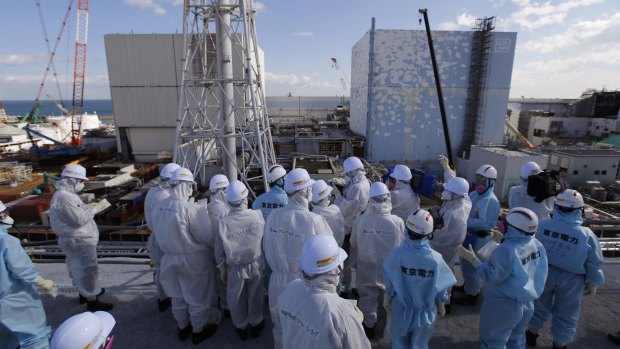 Members of a media tour group, wearing protective suits and masks, receive a briefing from  TEPCO employees (in blue) in front of the No. 1 and No. 2 reactor buildings at the Fukushima No. 1 nuclear power plant on Wednesday. 