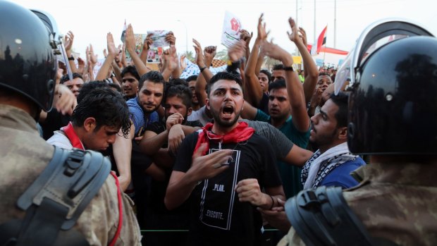 Protesters chant anti-government slogans while riot police guard the provincial council building during a protest against corruption and the lack of government services and power outage in Basra.