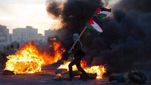 A Palestinian protester in Ramallah flies Palestinian flags during clashes with Israeli troops.