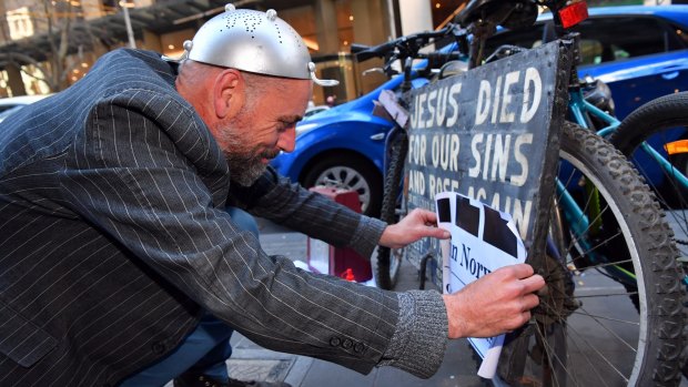 John McKenzie (aka IG McSporren) pastes a sign over a Jesus bike in the city.