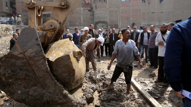 Egyptian workers lift parts of the statue with an excavator.