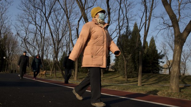 A woman wears a mask at a park as blue sky returns after heavy smog enveloped Beijing. 