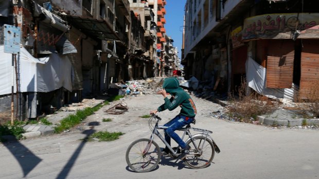 A Syrian boy covers his face as he rides a bicycle through a devastated part of the old city of Homs.