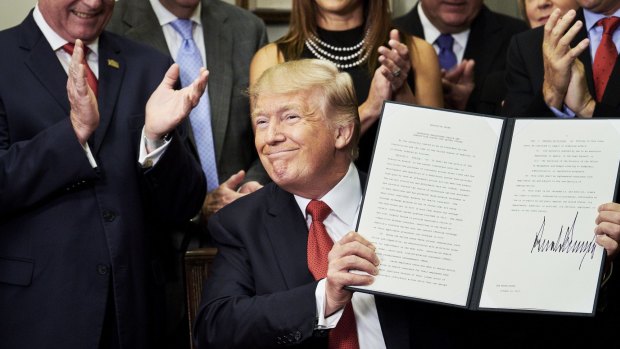 US President Donald Trump holds up a signed executive order on health care designed to expand health insurance options for some Americans, in a move that may also undermine coverage for those who remain in Obamacare.