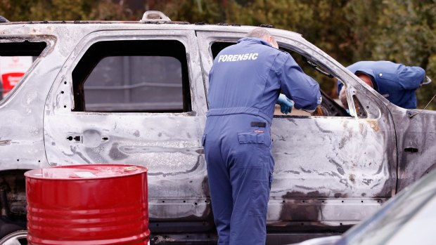 Forensic investigators inspect the burnt out vehicle.