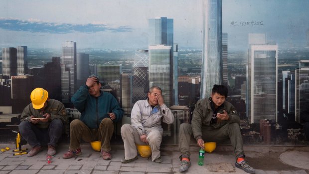 Construction workers rest near a board with an artist's impression of the Central Business District outside a construction site in Beijing.