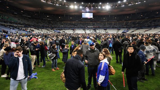 Terrified: Spectators gather on the pitch at Stade de France after news of the bombing and terrorist attacks reached the fans.