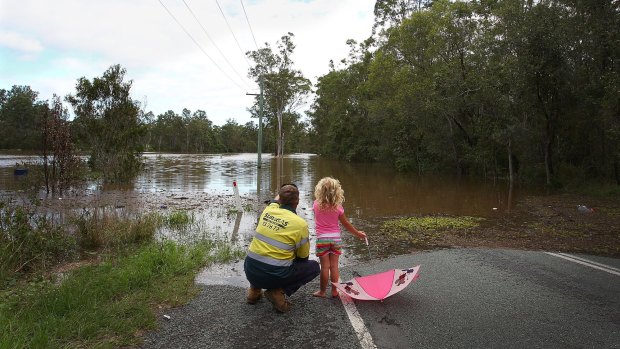 Adam Nelson and daughter Chloe, 5, look out at floodwater near their home outside Jimboomba.