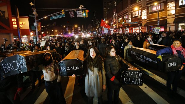 Protesters rallying against a grand jury's decision not to indict the police officer involved in the death of Eric Garner sing as they carry a collection of mock coffins bearing the names of victims of fatal police encounters in Brooklyn.