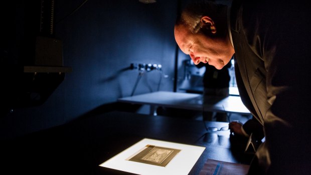 Senator George Brandis looks at photographic negatives from 1913