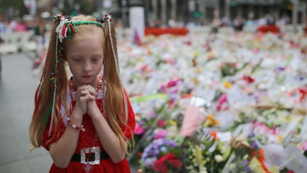 One year anniversary: A young girl dressed for Christmas attire walks around the thousands of floral tributes left in Martin Place a few days after the  siege.