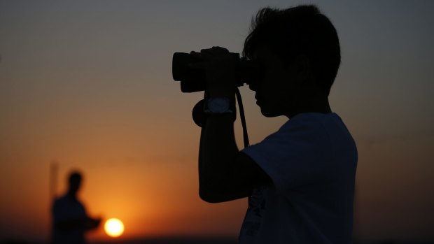 A teenage boy uses binoculars to look at Turkish army tanks holding positions near the border with Syria.