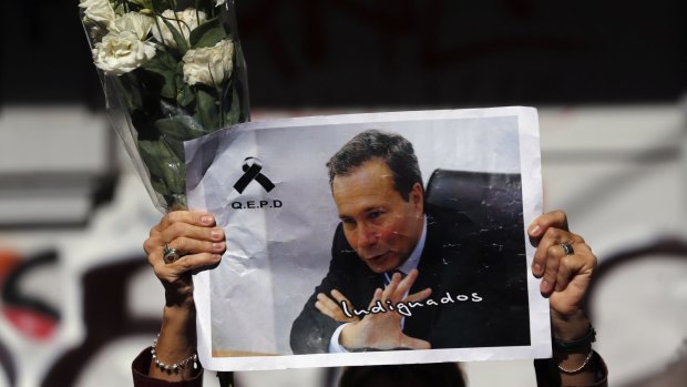 A woman holds up flowers and an image of late prosecutor Alberto Nisman.