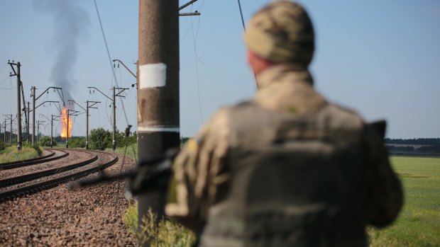 A Ukrainian soldier stands guard as flames erupt in the distance from a gas pipeline damaged by shelling.