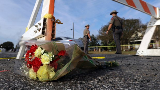 A bouquet of flowers lies at the base of a roadblock where law enforcement officials work at the scene of the shooting