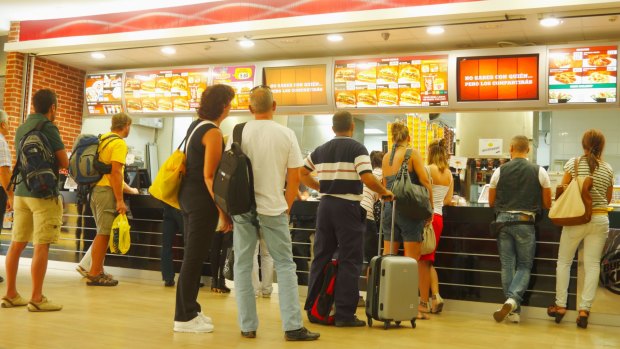 Passengers queue for fast food at the airport, where pricing is consistent.
