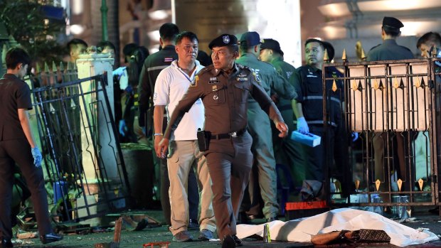 A police officer walks by the body of a victim covered in a white sheet following an explosion at the Ratchaprasong intersection in Bangkok.