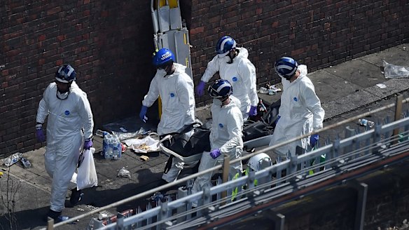 Police forensics carry a stretcher with a body bag out of the 24-storey residential Grenfell Tower block.